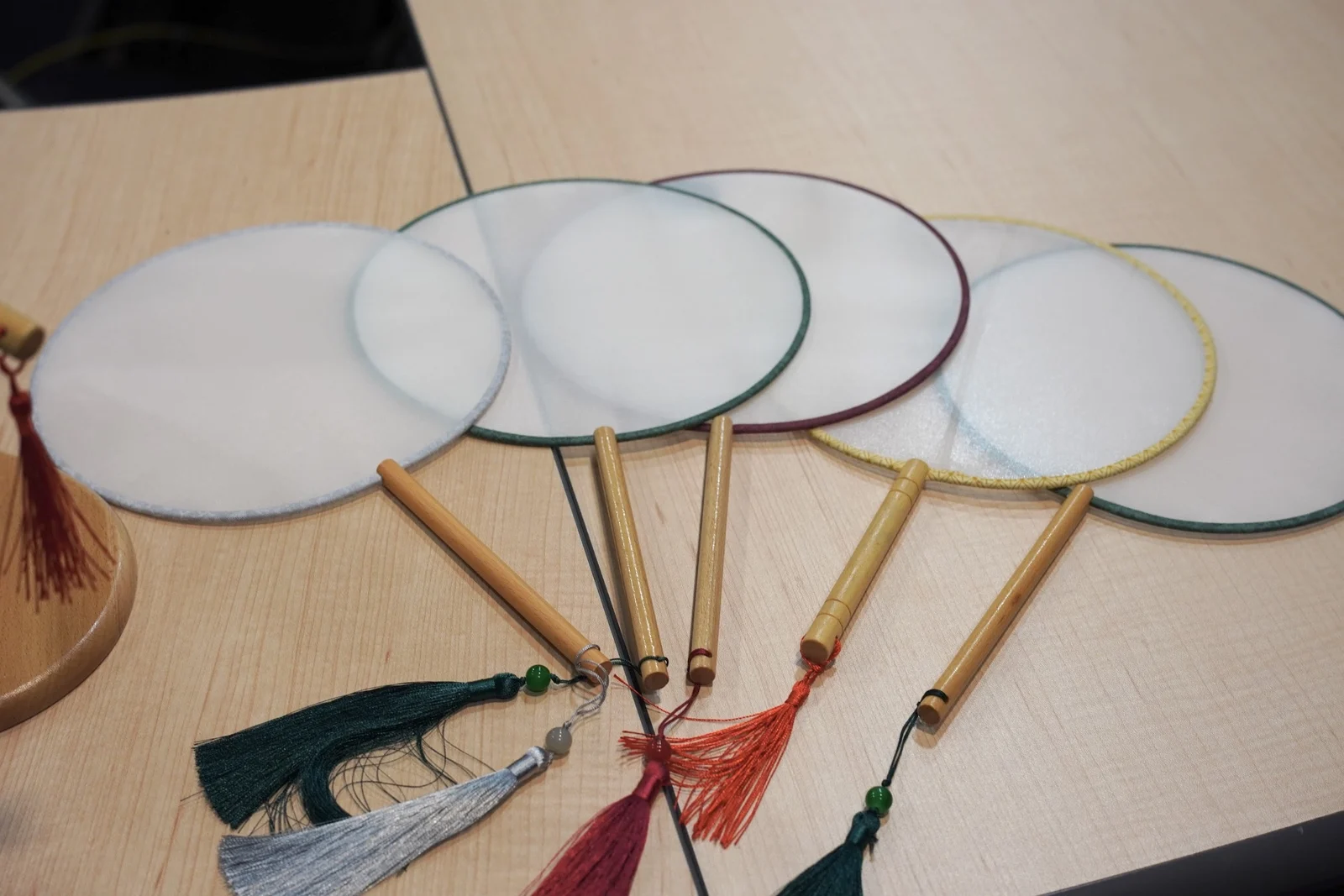 Round silk embroidery fans with wooden handles and colourful silk tassels arranged on a table.