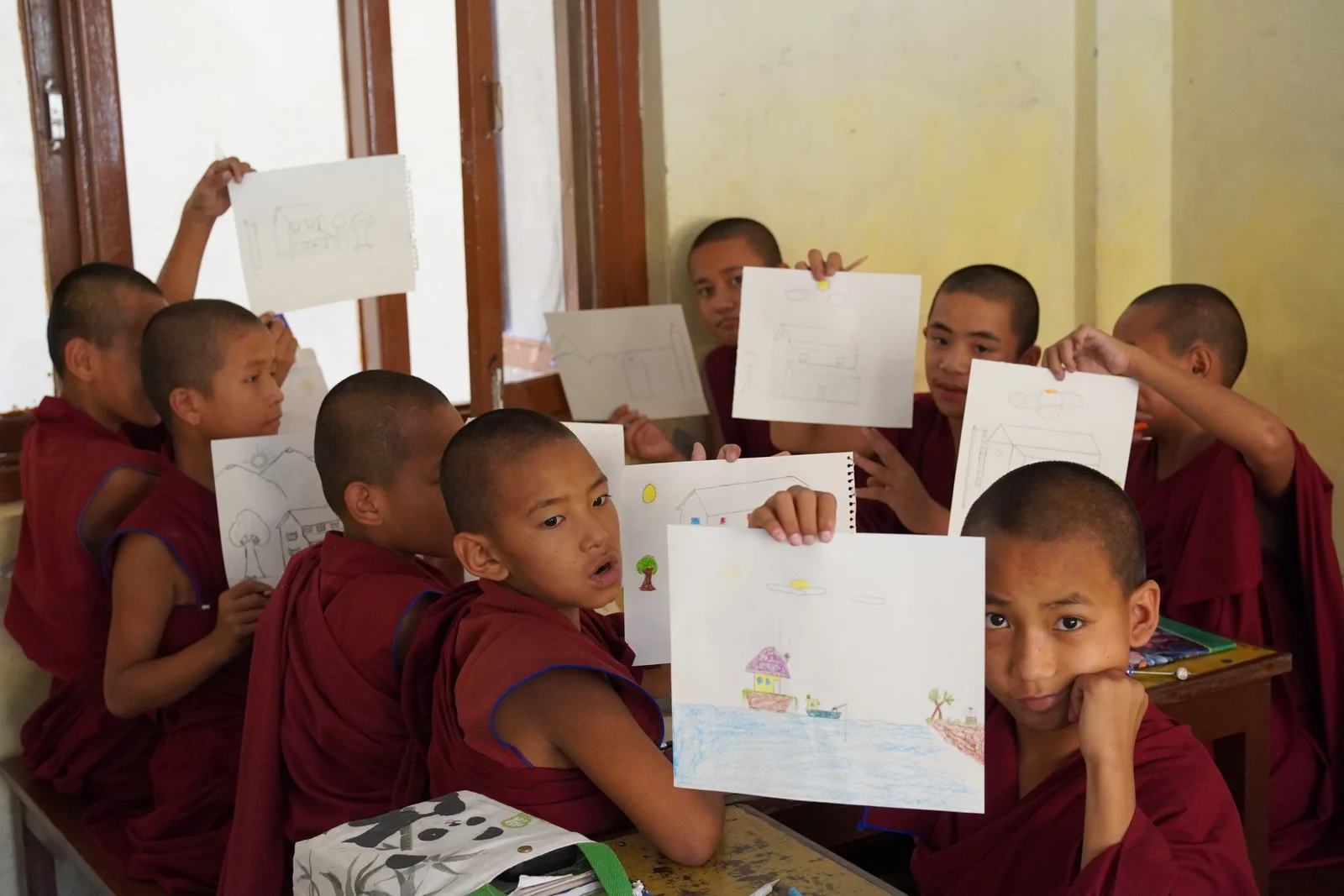 Children in a classroom holding up their drawings for the camera.