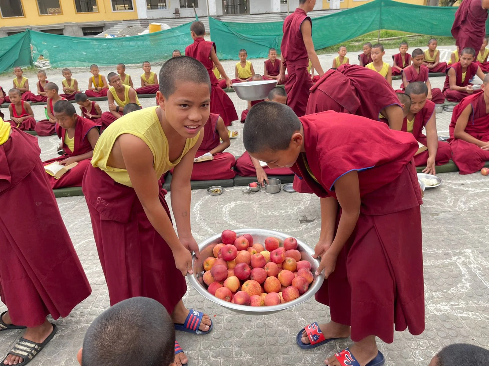 Two children carrying a basin of apples during an outdoor meal.