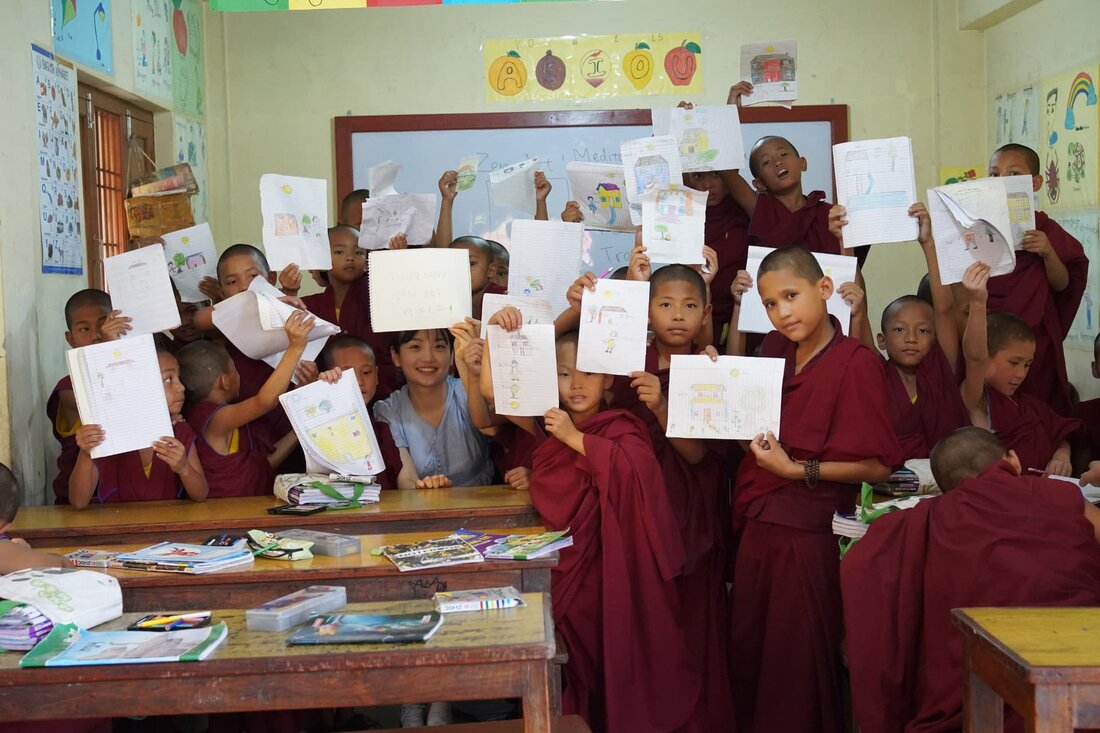 The facilitator surrounded by a large group of children holding up their drawings.
