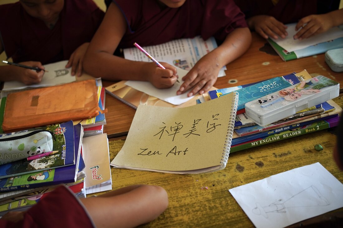 Children drawing at a classroom desk beside a notebook labelled Zen Art.